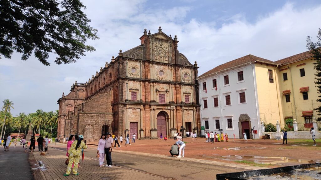 A historic Old Goa church with grand colonial-era architecture, featuring whitewashed walls, arched windows, and an ornate bell tower.